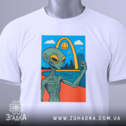 Футболка неземний вайб, біла, складена на столі, фон світло-сірий, принт з інопланетянином, що робить селфі, з етикеткою на рукаві.