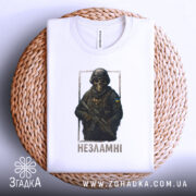 Футболка незламні воїни, біла, зображена в горизонтальному положенні на плетеній основі, на фоні світло-сірого градієнту, принт з зображенням воїна в масці та бронежилеті, з написом 'Незламні' під ним.