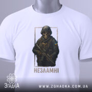 Футболка незламні воїни, біла, зображена в горизонтальному положенні, на фоні світло-сірого градієнту, принт з зображенням воїна в масці та бронежилеті, з написом 'Незламні' під ним, з етикеткою на шнурку.