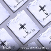 Футболка незламність духу, білого кольору, зображена на манекені з блискучою поверхнею, фон нейтральний, принт чорного кольору з зображенням хреста та написом 'Незламність духу'.