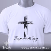 Футболка незламність духу, білого кольору, складена на столі, фон світлий, принт чорного кольору з зображенням хреста та написом 'Незламність духу', на комірці видна етикетка.