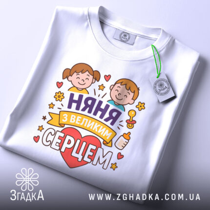 Футболка няня, білого кольору, зображена зверху, складена на поверхні, фон світло-сірий, принт з двома дітьми, серцем та написом 'няня з великим серцем', на комірці видна етикетка.