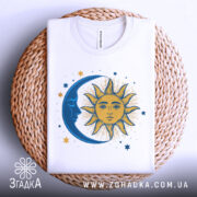 Футболка ніч і день, біла, зображена зверху, на фоні світлого плетеного кошика, з принтом, що зображає сонце та місяць, сонце жовтого кольору з деталями, а місяць синій.