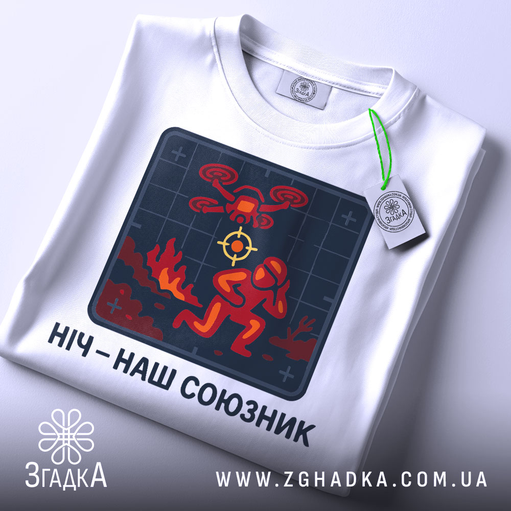 Футболка ніч наш союзник, білого кольору, зображена зверху, фон світло-сірий, принт з червоним і жовтим малюнком, що зображає людину в шоломі та дрон, на комірці є етикетка з зеленим шнурком.