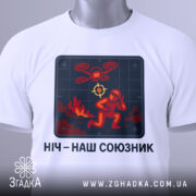 Футболка ніч наш союзник, білого кольору, зображена зверху, фон світло-сірий, принт з червоним і жовтим малюнком, що зображає людину в шоломі та дрон, на комірці є етикетка з зеленим шнурком.