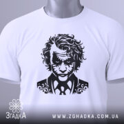 Футболка нічний бунтар, біла, складена на столі, з видимим етикеткою зеленого кольору, фон світло-сірий, принт з чорним малюнком обличчя персонажа з кучерявим волоссям і костюмом.