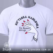 Футболка нігтьова маньячка, білого кольору, складена на поверхні, фон світло-сірий, принт з рукою з червоними нігтями та написом 'До ваших послуг', на комірці видна етикетка.