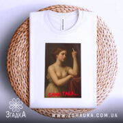 Футболка ніжність провокує, біла, зображена зверху на плетеному кошику, на фоні світлого кольору, принт з класичним зображенням жінки, що показує середній палець, з червоним написом 'САМА ТАКА....'.