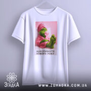 Футболка новорічний грінч, біла, зображена з фронтального ракурсу, фон світло-сірий, принт з грінчем у рожевому халаті, який жує жувальну гумку, текст "Щасливого Нового Року" під малюнком.