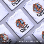 Футболка новорічний кінь, біла, зображена з фронтального ракурсу, фон світло-сірий, принт з веселим кінем, що стрибає через цегляну стіну, текст "З НОВИМ РОКОМ" під принтом.