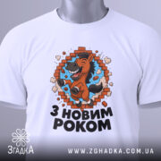 Футболка новорічний кінь, біла, складена на поверхні, фон світло-сірий, принт з кінем, що стрибає через цегляну стіну, текст "З НОВИМ РОКОМ" під принтом, на комірці є етикетка.