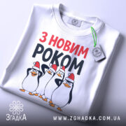Футболка новий рік пінгвіни, біла, з верхнього ракурсу, на столі, фон світлий, принт з чотирма пінгвінами у червоних новорічних шапках, текст 'З НОВИМ РОКОМ' у червоному та чорному кольорах, з зеленим ярликом.