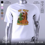 Футболка ну що святкуємо, біла, зображена з фронтального ракурсу, на фоні світлого градієнту, принт з веселим конем у червоній шапці, що тримає келих з шампанським на фоні ялинки.