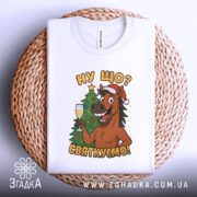 Футболка ну що святкуємо, біла, зображена зверху на плетеній основі, принт з усміхненим конем у червоній шапці, що тримає келих з шампанським, поряд ялинка.