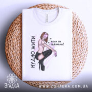 Футболка нудно жити, біла, складена на плетеному кошику, фон світло-сірий, принт з дівчиною в чорних колготах і написом зліва.