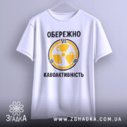 Футболка обережно кавоактивність, білого кольору, підвішена на вішалці, фон світло-сірий, принт жовтого кольору з символом радіації та текстом, видно деталі крою.