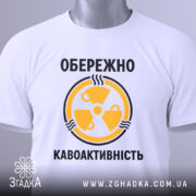 Футболка обережно кавоактивність, білого кольору, складена на поверхні, фон світло-сірий, принт жовтого кольору з символом радіації та текстом, на комірці видна етикетка.