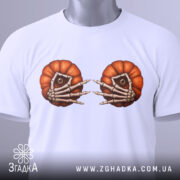 Футболка очі гарбуза, біла, складена на столі, фон світло-сірий, принт з двома гарбузами з очима та скелетними руками, на футболці є етикетка з зеленим шнурком.