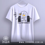 Футболка один крякає. Біла футболка, підвішена на вішалці, з принтом качки, що крякає, та текстом "Один крякає – інші мовчать!". Фон світло-сірий.