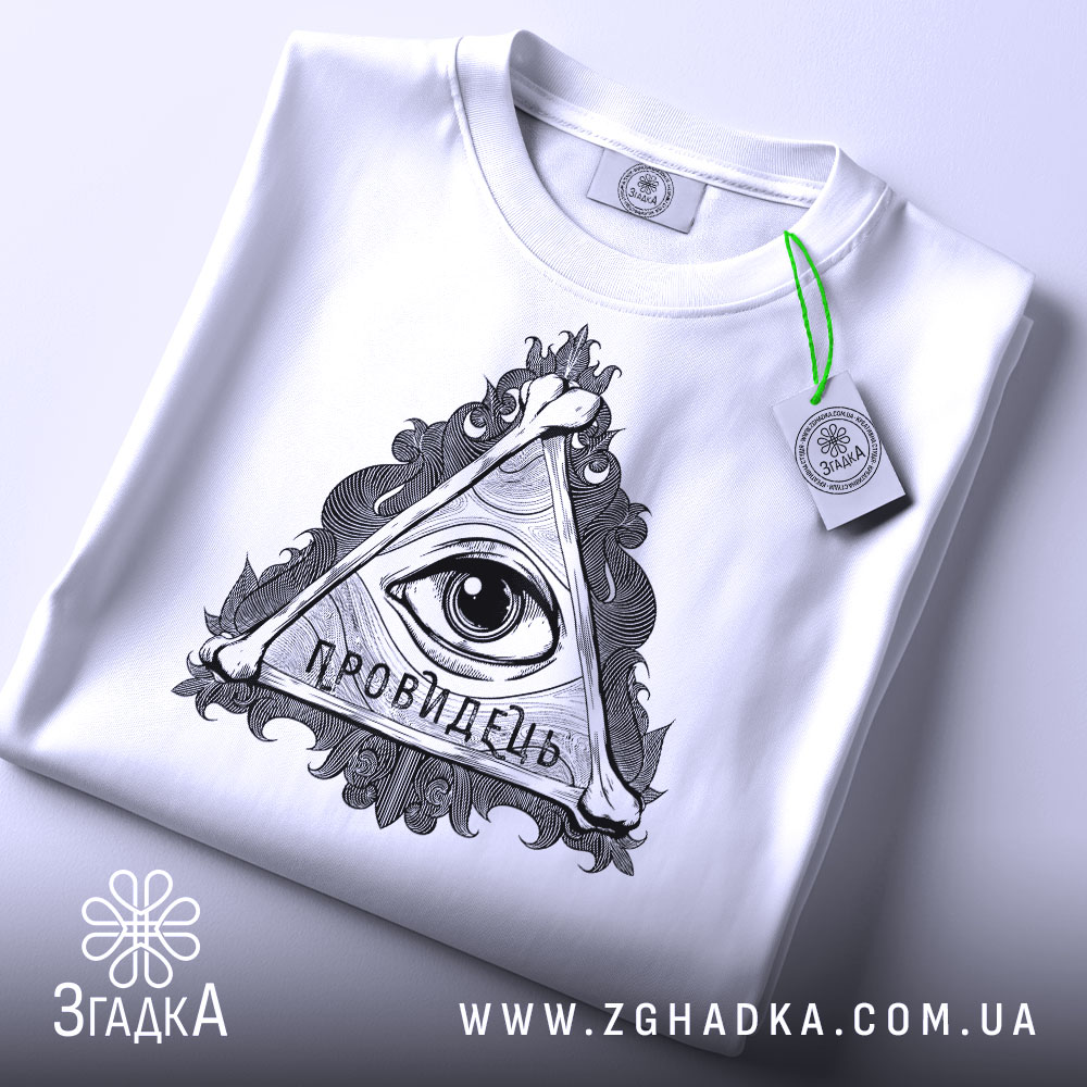 Футболка око провидця, біла, складена на поверхні, фон світло-сірий, принт у вигляді трикутника з оком та написом 'ПРОВИДЕЦЬ', на футболці є етикетка з зеленим шнурком.