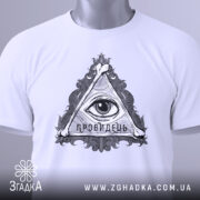 Футболка око провидця, біла, складена на поверхні, фон світло-сірий, принт у вигляді трикутника з оком та написом 'ПРОВИДЕЦЬ', на футболці є етикетка з зеленим шнурком.