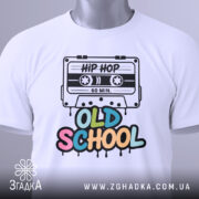 Футболка Old School білого кольору, складена на поверхні, з видимим етикеткою, фон світлий, принт з касетою та написом 'OLD SCHOOL' у яскравих кольорах.
