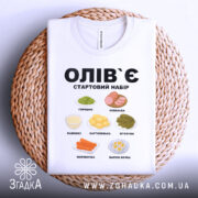 Футболка олів`є набір білого кольору, складена на плетеній кошику, фон білий, принт містить малюнки овочів та інгредієнтів олів`є, текст чорного кольору: 'ОЛІВ`Є СТАРТОВИЙ НАБІР'.