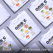 Футболка олів`є набір білого кольору, зображена на манекені з правого боку, фон світло-сірий, принт містить малюнки овочів та інгредієнтів олів`є, текст чорного кольору: 'ОЛІВ`Є СТАРТОВИЙ НАБІР'.