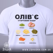 Футболка олів`є набір білого кольору, складена на поверхні, фон світло-сірий, принт містить малюнки овочів та інгредієнтів олів`є, текст чорного кольору: 'ОЛІВ`Є СТАРТОВИЙ НАБІР', на футболці є етикетка зеленого кольору.