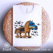 Футболка операція павутина подарунок. Біла футболка, складена на плетеній основі, з принтом, що зображує Троянського коня та вантажівку. Фон світло-сірий, деталі принта яскраві, з літаками, що оточують коня.