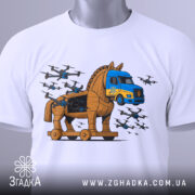 Футболка операція павутина подарунок. Біла футболка, складена на столі, з принтом, що зображує Троянського коня та вантажівку. На футболці видно етикетку з зеленим шнурком. Фон світло-сірий, деталі принта яскраві, з літаками.