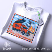 Футболка операція павутина, біла футболка, складена на поверхні, принт з червоним вантажівкою, дронами та вогнем, напис 'Свято Наближається' на фоні блакитного неба, прикріплена етикетка з зеленим шнурком.