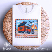 Футболка операція павутина, біла футболка, складена на плетеній основі, принт з червоним вантажівкою, дронами та вогнем, напис 'Свято Наближається' на фоні блакитного неба.