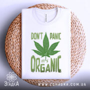 Футболка органік стиль канабіс, біла, складена на плетеній кошику, фон білий, принт зелений з написом 'DON'T PANIC it's ORGANIC' та зображенням листа канабісу.