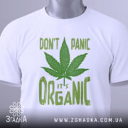 Футболка органік стиль канабіс, біла, складена на поверхні, фон світло-сірий, принт зелений з написом 'DON'T PANIC it's ORGANIC' та зображенням листа канабісу, з етикеткою на комірці.