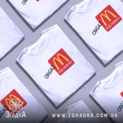 Футболка оргазм я це люблю, біла футболка з принтом, на якому зображено логотип McDonald's у червоному квадраті, текст 'ORGAZ' написаний чорним шрифтом, фон нейтральний, футболка на манекені.