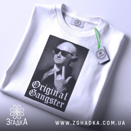 Футболка оригінальний ґангстер білого кольору, складена на поверхні, з видимим етикеткою, фон світло-сірий, принт з зображенням чоловіка в окулярах, який показує жест, з написом 'Original Gangster' під ним.