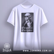 Футболка оригінальний ґангстер білого кольору, підвішена на вішалці, фон світло-сірий, принт з зображенням чоловіка в окулярах, який показує жест, з написом 'Original Gangster' під ним.