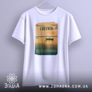 Футболка озеро Світязь, біла, підвішена на вішалці, фон світло-сірий, принт з малюнком озера, човна та сонця, текст на принті зеленого кольору.