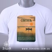 Футболка озеро Світязь, біла, складена на поверхні, фон світло-сірий, принт з малюнком озера, човна та сонця, текст на принті зеленого кольору, з етикеткою з зеленим шнурком.