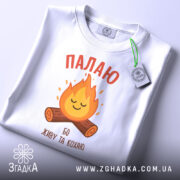 Футболка палаю кохаю, біла, зображена з верхнього ракурсу, на фоні світло-сірого градієнту, принт з вогнем та колодами, на футболці є етикетка з зеленим шнурком.