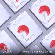 Футболка памʼятай своє коріння, білого кольору, зображена на манекені з правого ракурсу, фон нейтральний, принт містить червоне сонце, чорне дерево та птахів, текст під малюнком.