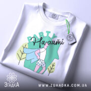 Футболка Party на хаті, біла, зображена зверху, фон світло-сірий, принт з малюнком хлопця в капелюсі з синім плащем та шортах з сердечками, напис 'Party' зверху, на футболці є етикетка.