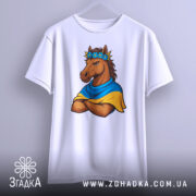 Футболка патріотичний кінь, біла, підвішена на вішалці, фон світло-сірий, принт з кінем у вінку з квітів та синьо-жовтому шарфі, кінь з серйозним виразом обличчя, руки схрещені на грудях.