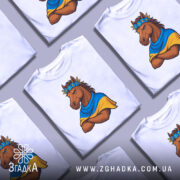 Футболка патріотичний кінь, біла, зображена на манекені, фон світло-сірий, принт з кінем у вінку з квітів та синьо-жовтому шарфі, кінь з серйозним виразом обличчя, руки схрещені на грудях.