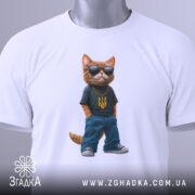 Футболка патріотичний кіт, біла, зображена з верхнього ракурсу, на фоні світло-сірого градієнту, принт з котом у темній футболці з жовтим гербом України та синіх штанах, в темних окулярах, з етикеткою на зеленому шнурку.
