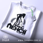 Футболка пенсія піски часу. Біла футболка, складена на плоскій поверхні, фон світло-сірий. Принт чорного кольору з силуетом людини з ходунками, текстом "Принц пенсії піски часу" під малюнком, на футболці є етикетка з зеленим шнурком.