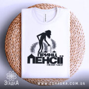 Футболка пенсія піски часу. Біла футболка, складена на плоскій поверхні, фон світлий. Принт чорного кольору з силуетом людини з ходунками, текстом "Принц пенсії піски часу" під малюнком, футболка розташована на плетеній основі.