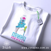 Футболка пенсійний жарт, біла, зображена з верхнього ракурсу, фон світло-сірий, принт з малюнком блакитного персонажа з банкою на голові, напис 'ПРИН!!! пенсії' у блакитному кольорі, на футболці є етикетка.