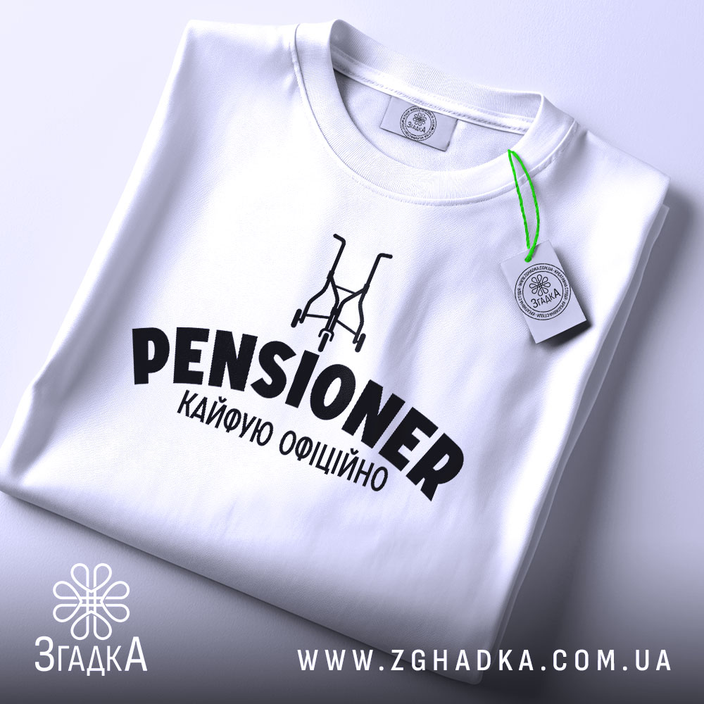 Футболка пенсіонер кайфую, біла, зображена зверху, на фоні світло-сірого кольору, з принтом чорного кольору, що містить слово 'PENSIONER' та малюнок візка, з етикеткою зеленого кольору.